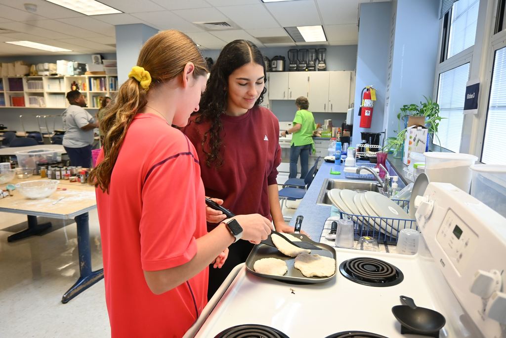 Two girls cook their pita on a griddle.
