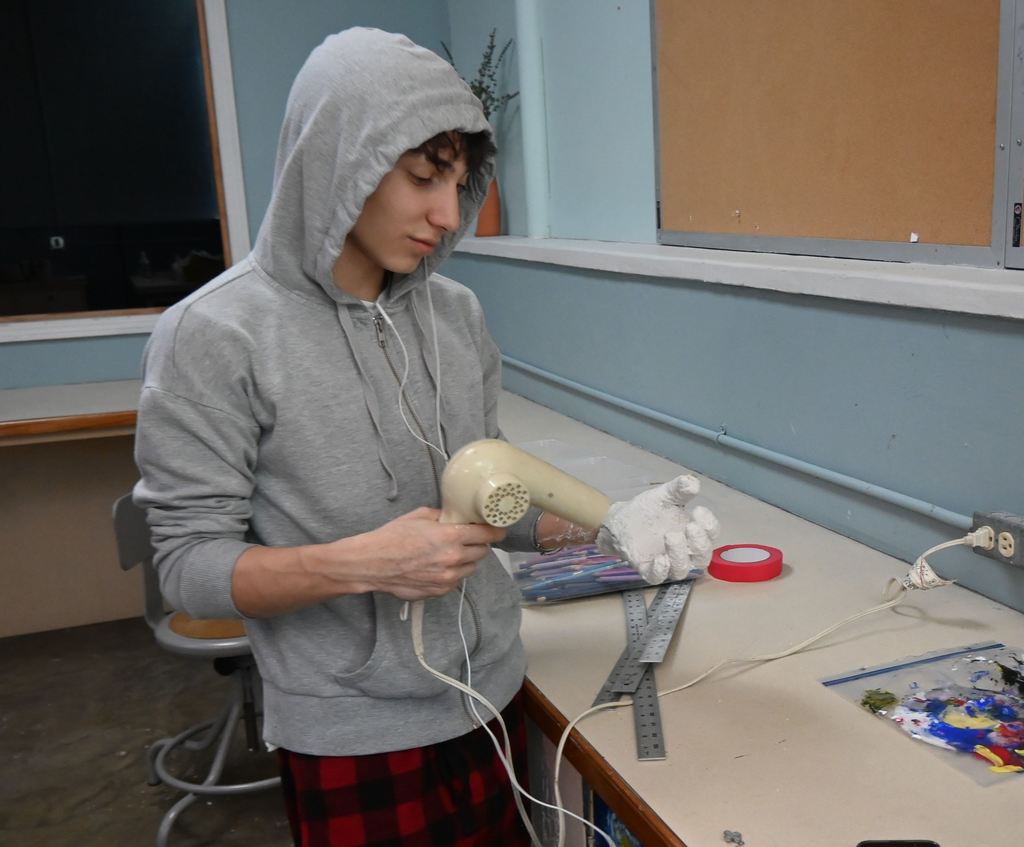 A students uses a blow dryer to dry the cast on his hand.
