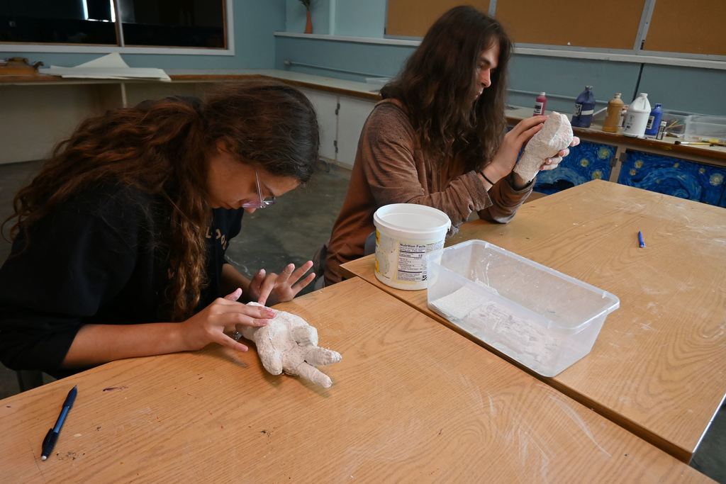 A boy and a girl do touch ups on the casts of their hands.