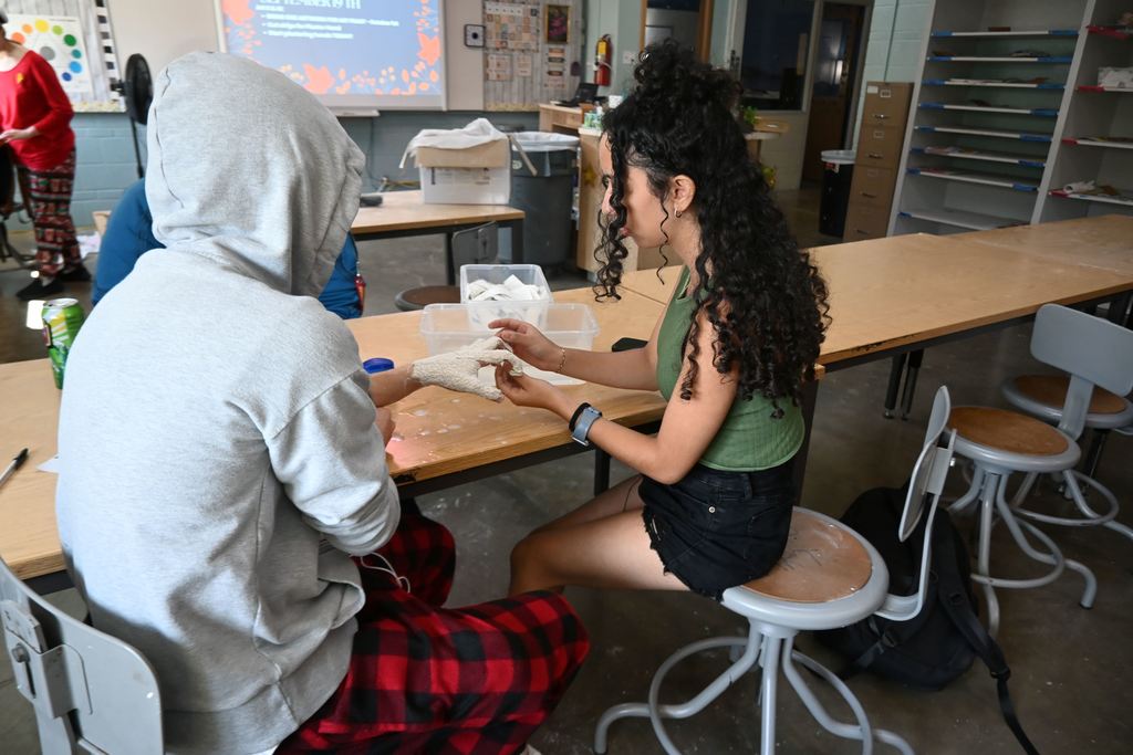 Two boys chat while a girl makes a cast of one of their hands.