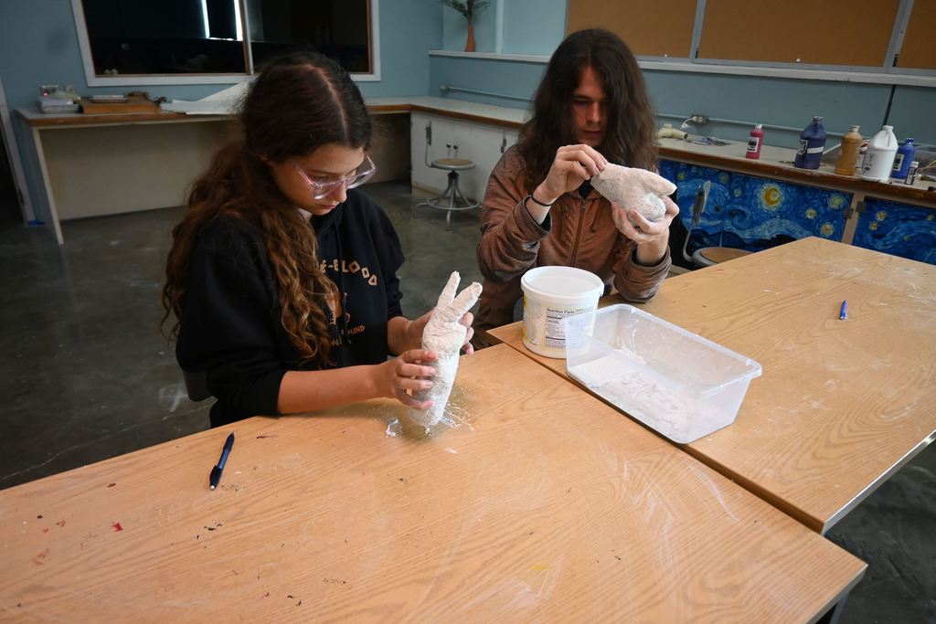 A boy and a girl do touch ups on the casts of their hands.