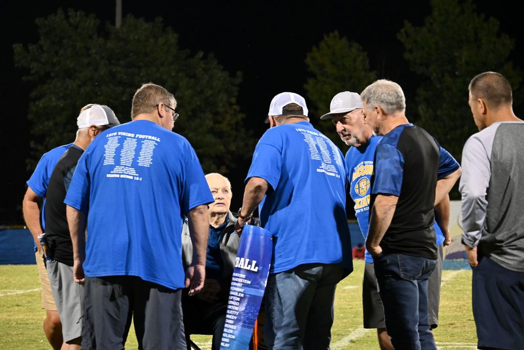 Members of the 1975 PHS football team gather on the field with former line coach Harley Turner.