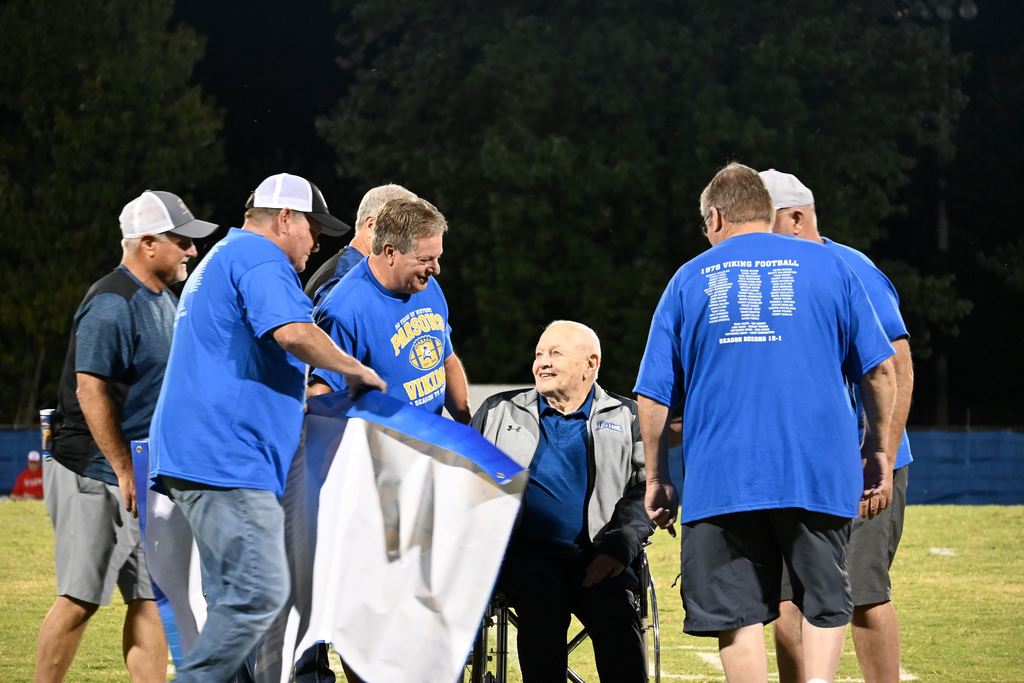 Members of the 1975 PHS football team gather on the field with former line coach Harley Turner.