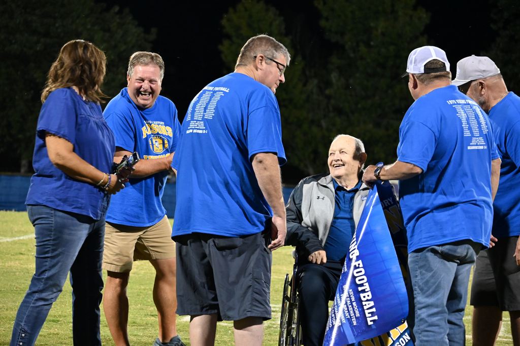 Members of the 1975 PHS football team gather on the field with former line coach Harley Turner.