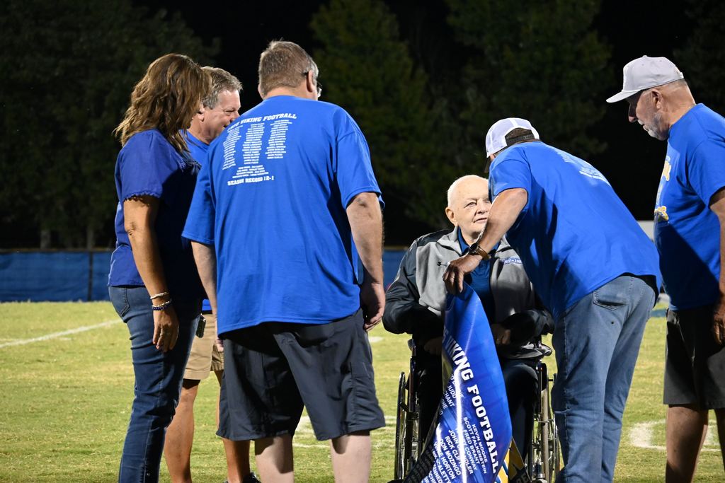 Members of the 1975 PHS football team gather on the field with former line coach Harley Turner.