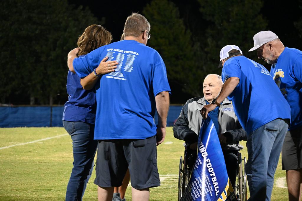 Members of the 1975 PHS football team gather on the field with former line coach Harley Turner.