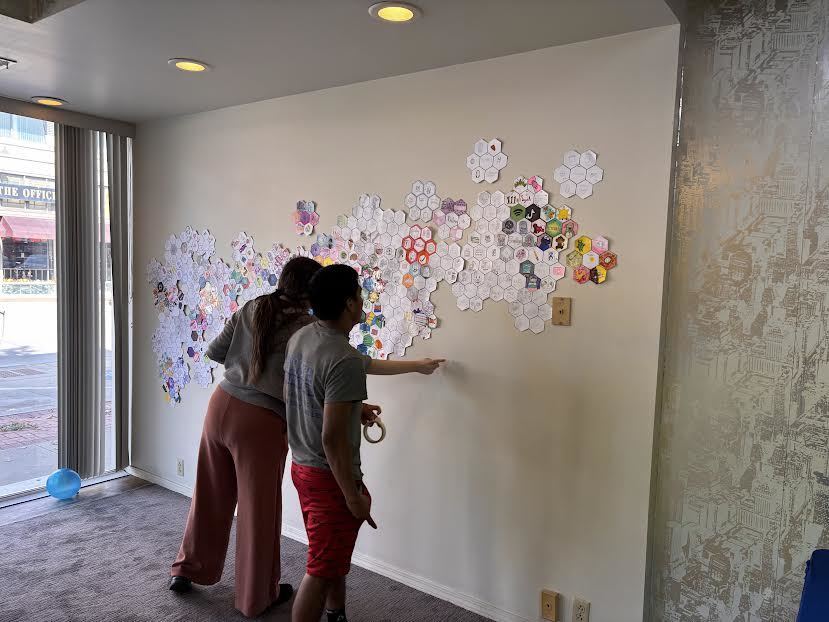 Students hang a mural made up of small individual pictures drawn by students.