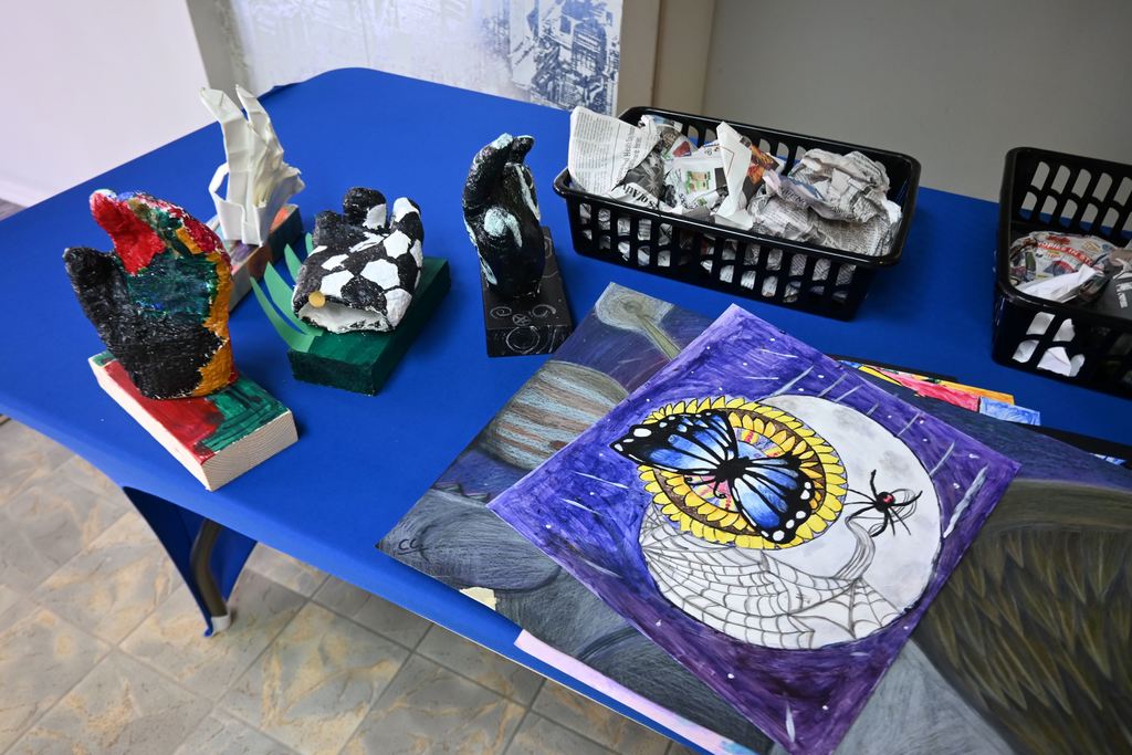 Baskets of ceramic art and stacks of pictures fill a table waiting to be displayed.