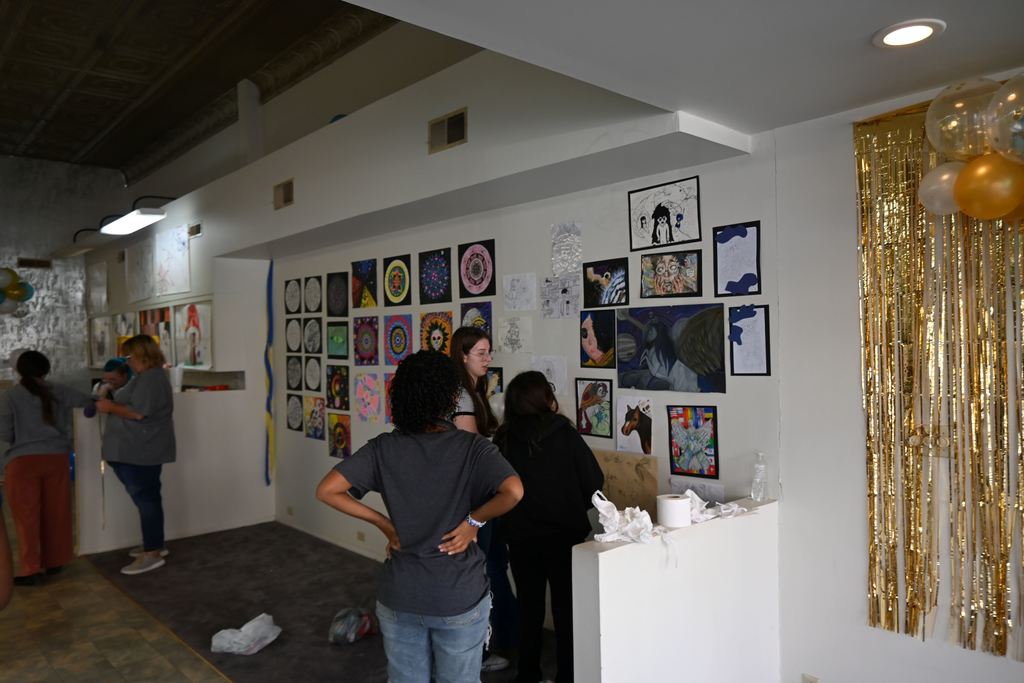 Students hang drawings and paintings on the wall.