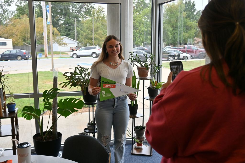 A senior gets her picture taken with her pennant listing one of several colleges she applied to.