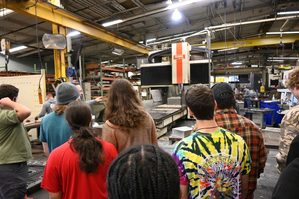 Students watch a machine cut a part out of a large block of titanium.