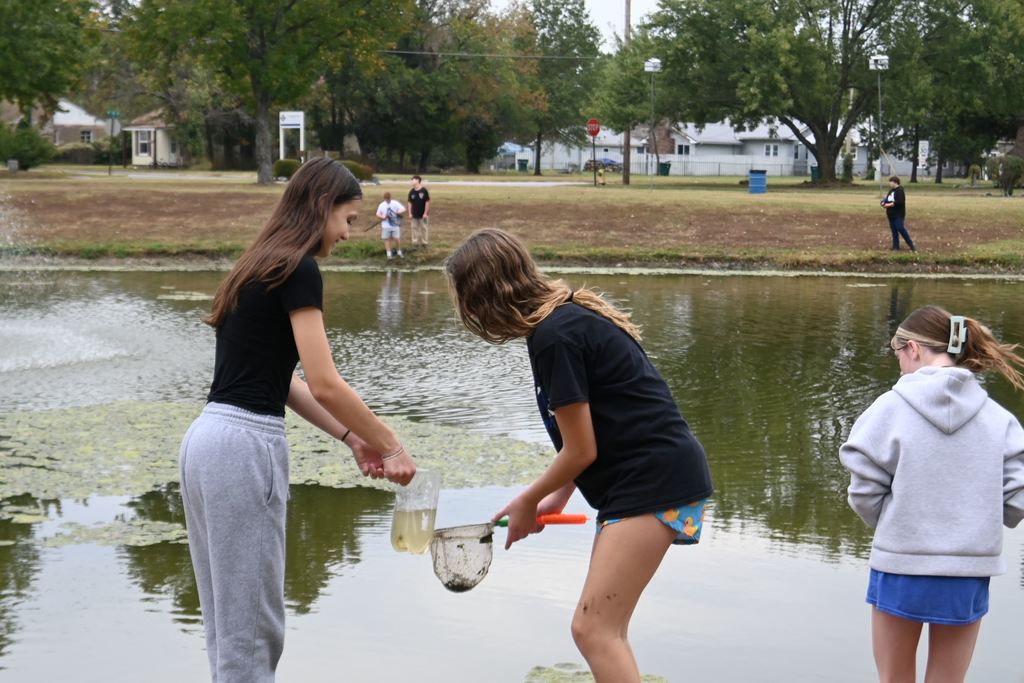 Two girls take things from the net and add them in their ecosystem container.