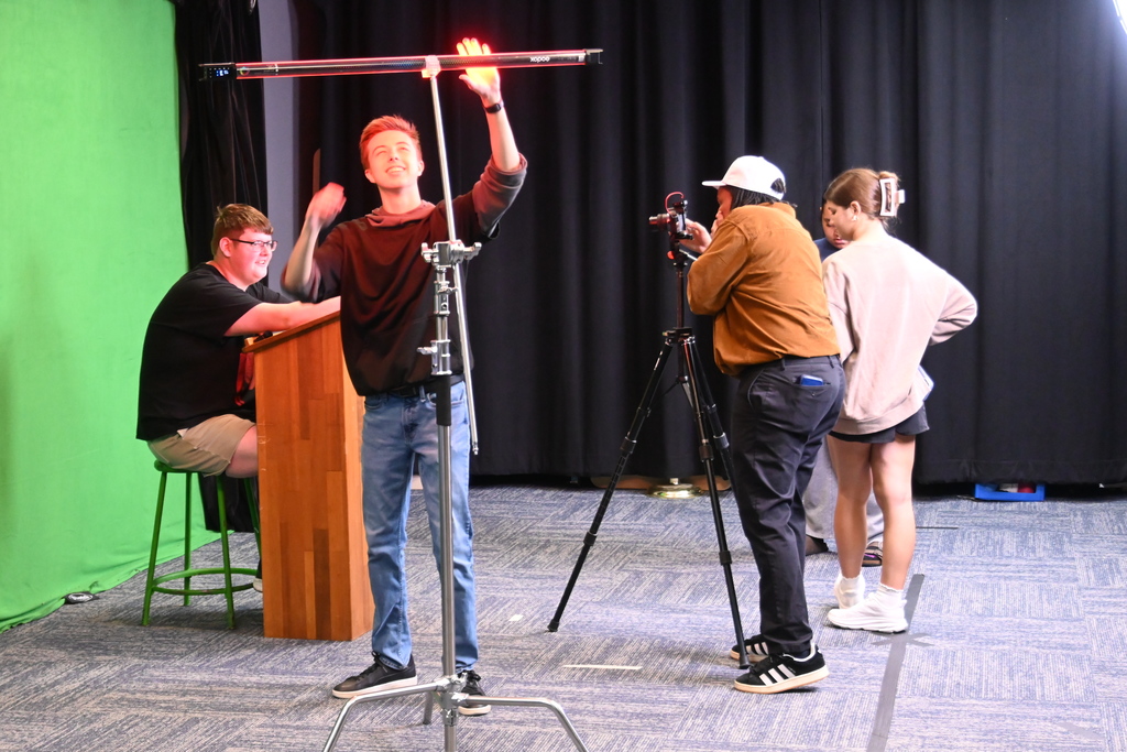 A student sets up another light while the teacher helps a student with the camera settings.