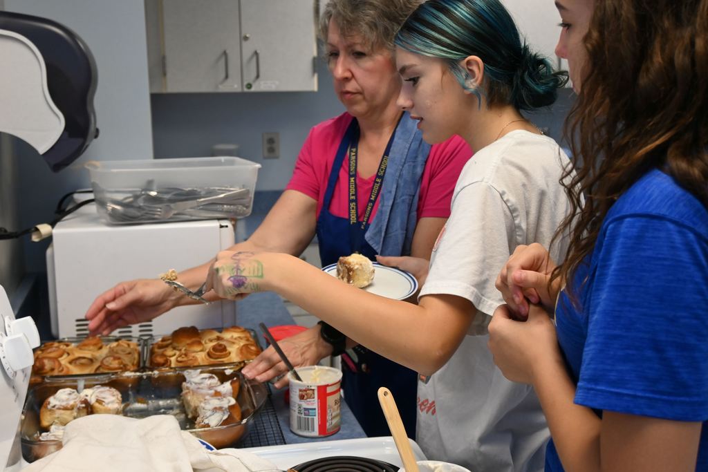 Students cut cinnamon rolls for visitors to the classroom.
