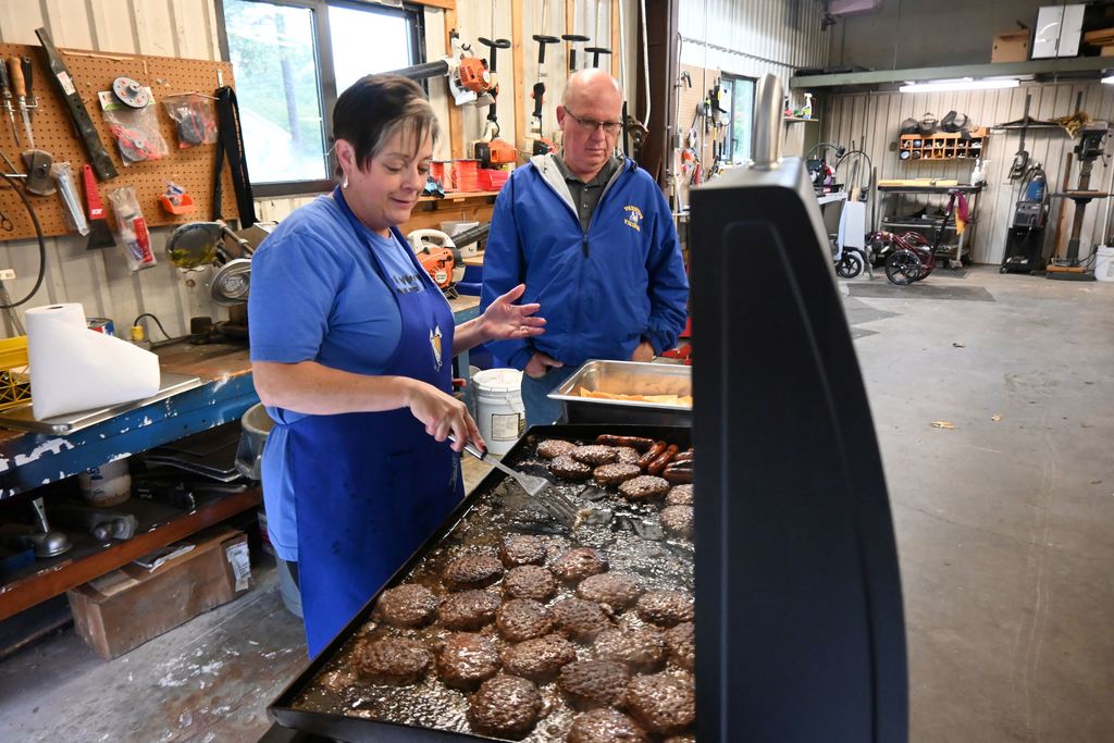 Lori Perkins flips burgers on the grill as Rick Giefer looks on.