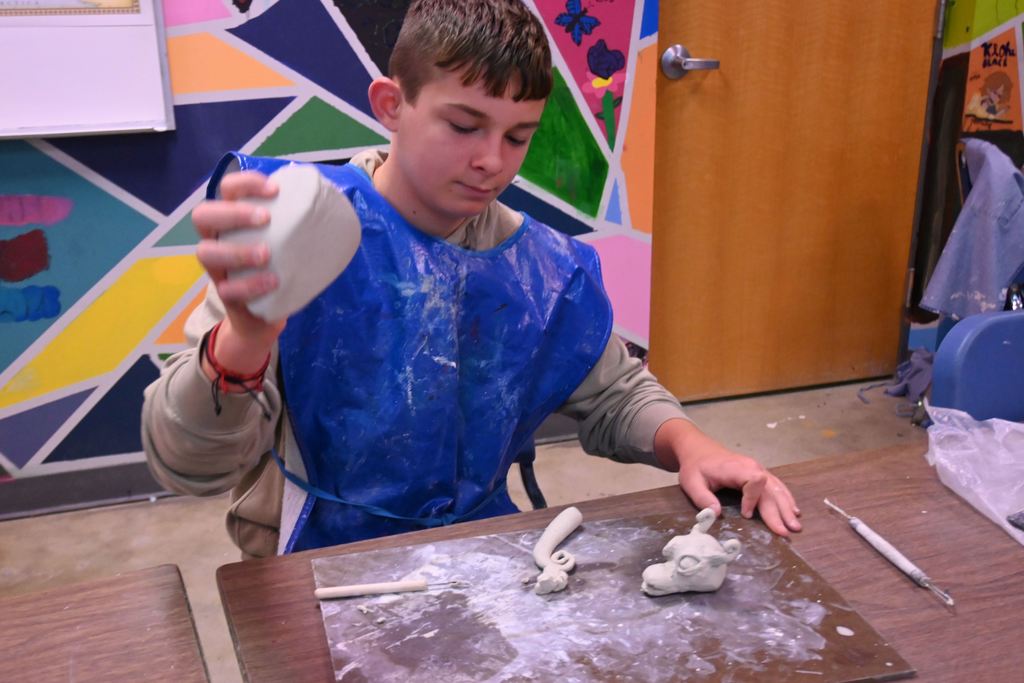 A student warms a ball of clay so he can finish the body of his dragon.