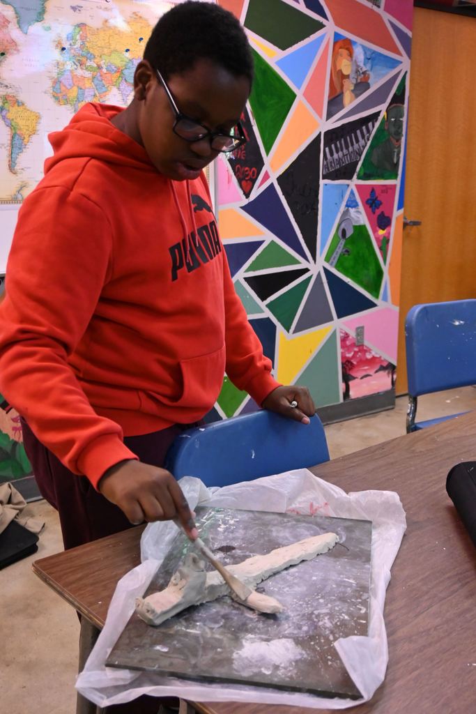 A student smooths the clay on his dragon's body.