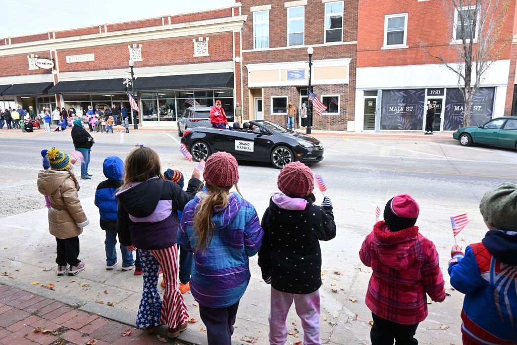 The Parade Grand Marshall waves at children  waving flags.