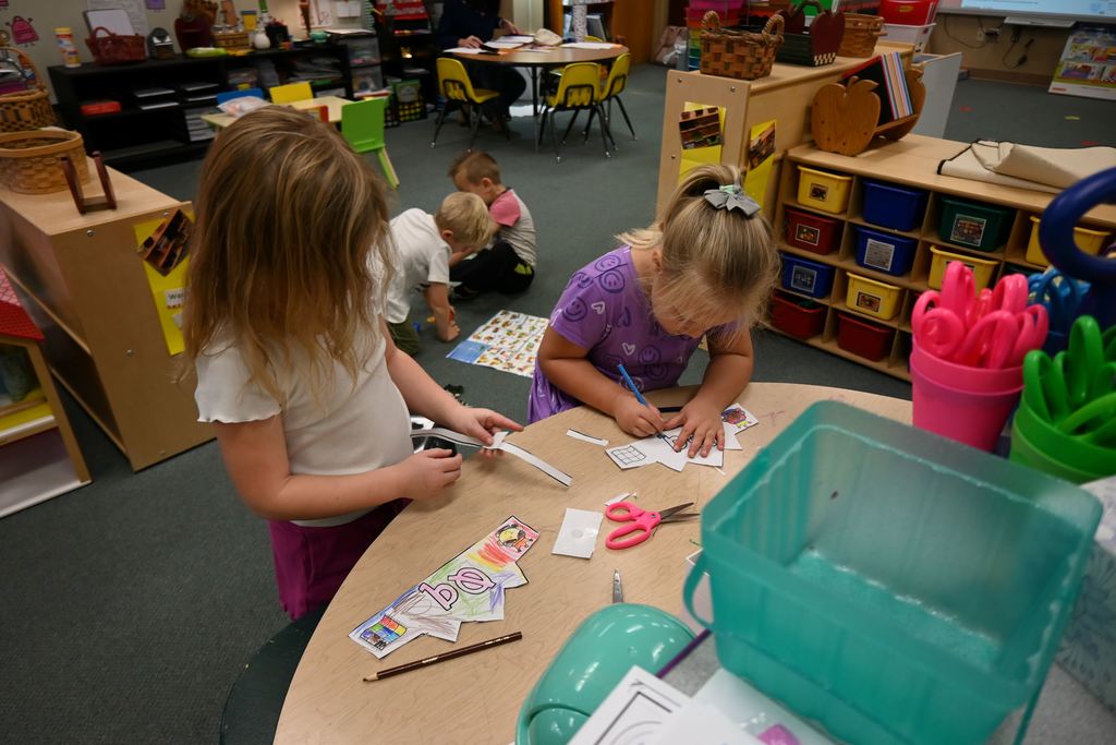 Two little girls  color and cut  papers about the letter Q.