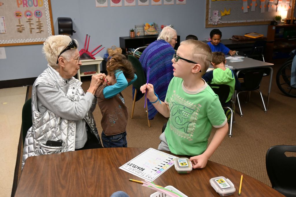 A woman from Presby helps a girl with her necklace while a boy visits with her about his bracelet.
