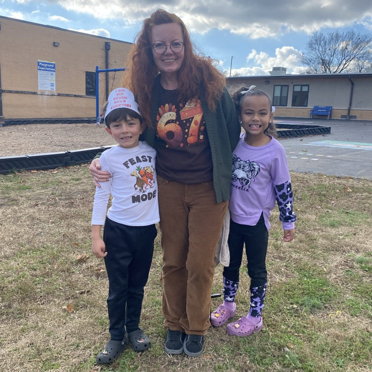 teacher in a 67 shirt posing with two students, one in a six seven days smarter headband