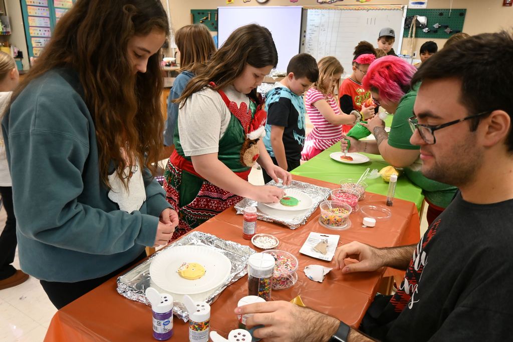 Two girls, assisted by Cody Homes, decorate their cookies with sprinkles.