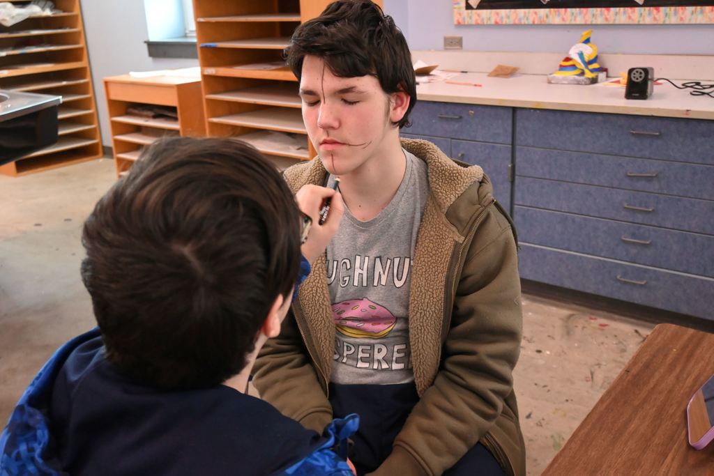 Students use eye liner to draw lines on one another's faces to define proportions and facial features.