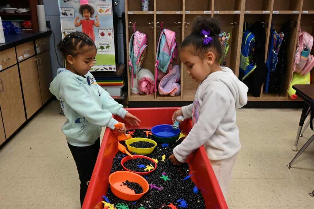 Two students play in a tub full of black beans.