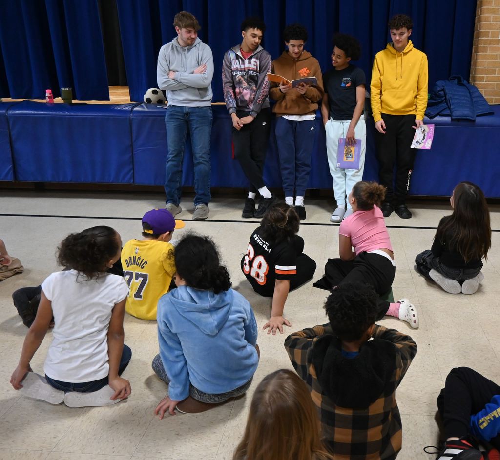 High School athletes read to a group of students in the gym.