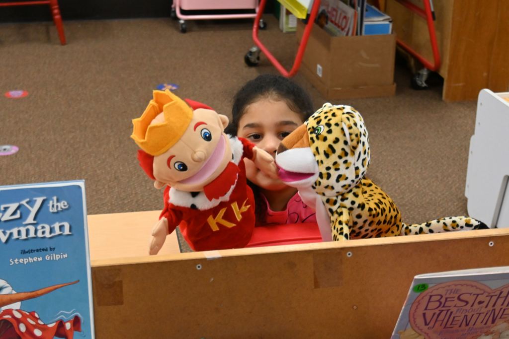 A little girl plays with a  king hand puppet and an leopard hand puppet.