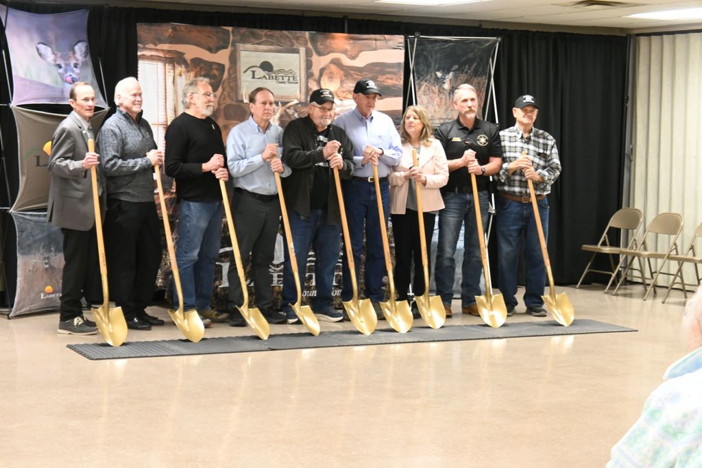 Due to rain Veterans and others involved in the memorial stand with shovels in the basement of the municipal building for the ground breaking ceremony.