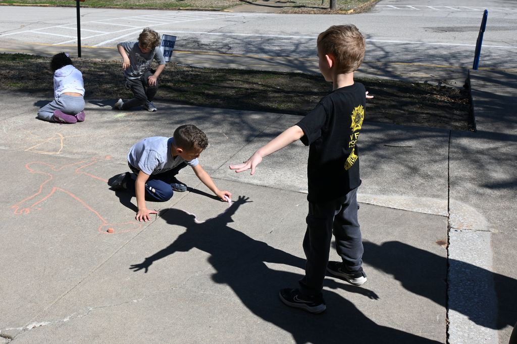 Pne student traces another student's shadow with chalk.