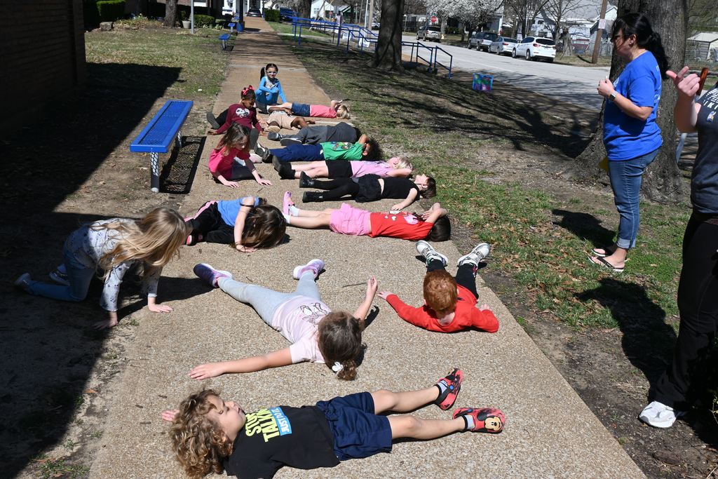 Students lay on the warm sidewalk in the sun,.