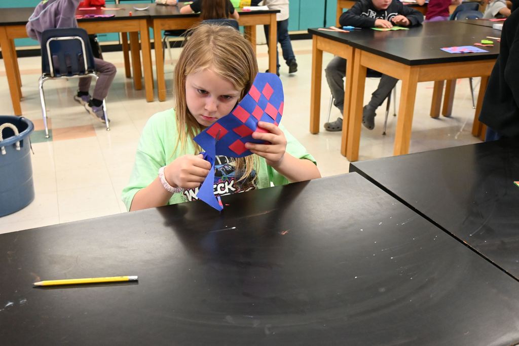 A little girl cuts out the shape of a fish body for her paper weave project.