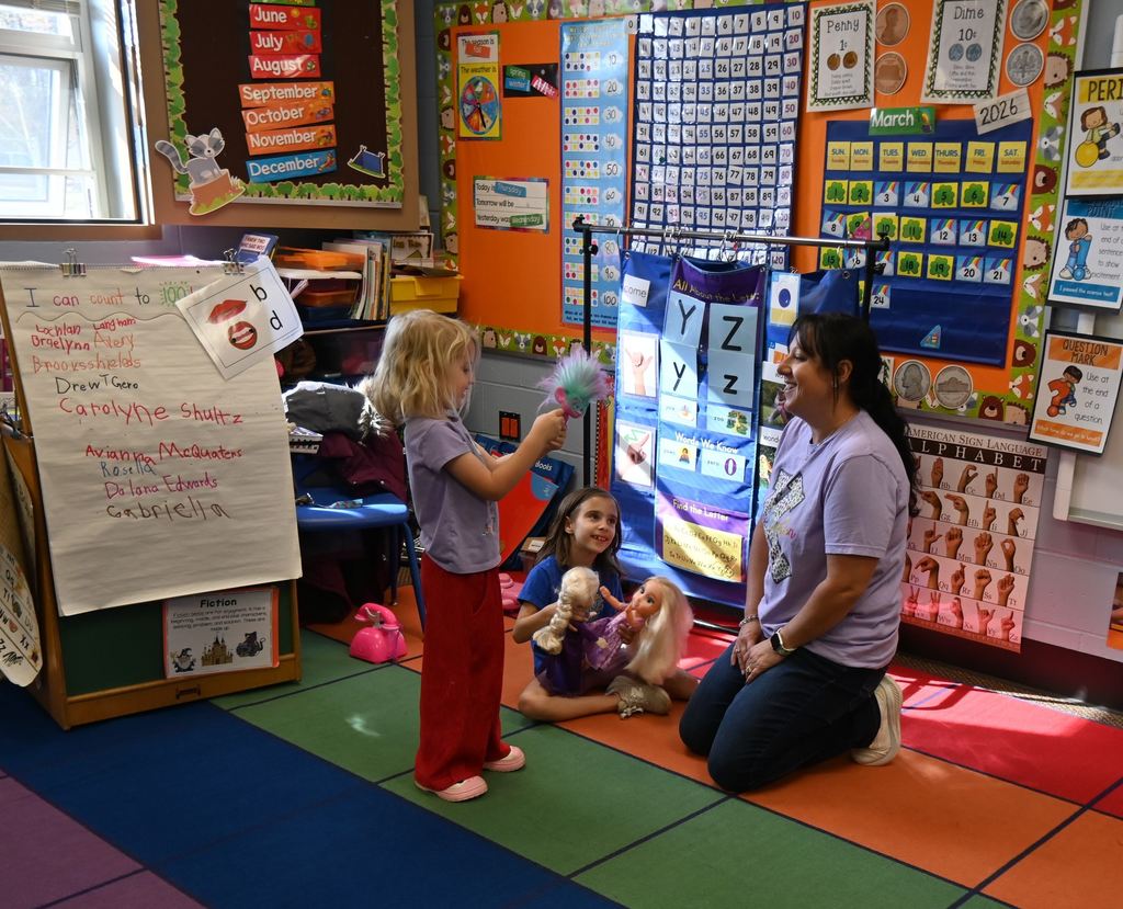 Mrs. Kennett cisits with two little girls in her classroom.