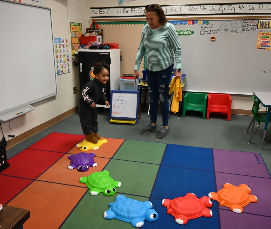 A little girl plays on turtle stepping stones as her mom watches.