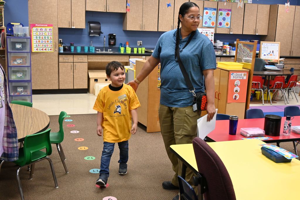 A grandmother walks around a kindergarten classroom with her grandson, checking things out.