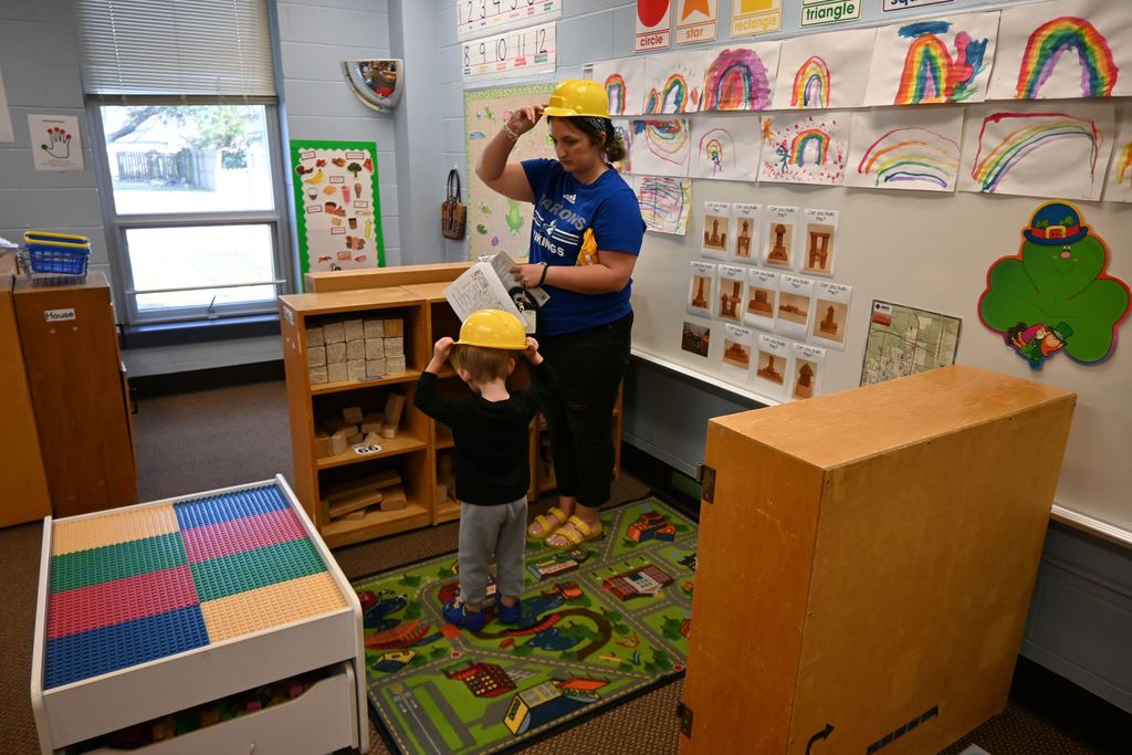 A mom puts on a construction hat with her son in a preschool play area .