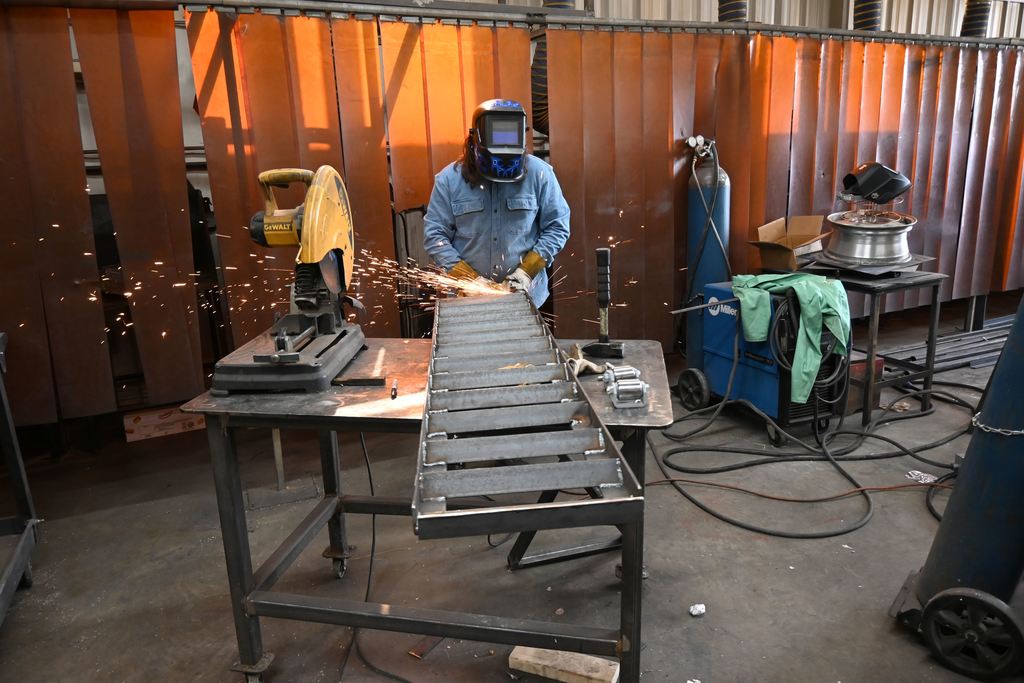 A student grinds on welds on a  trailer ramp
