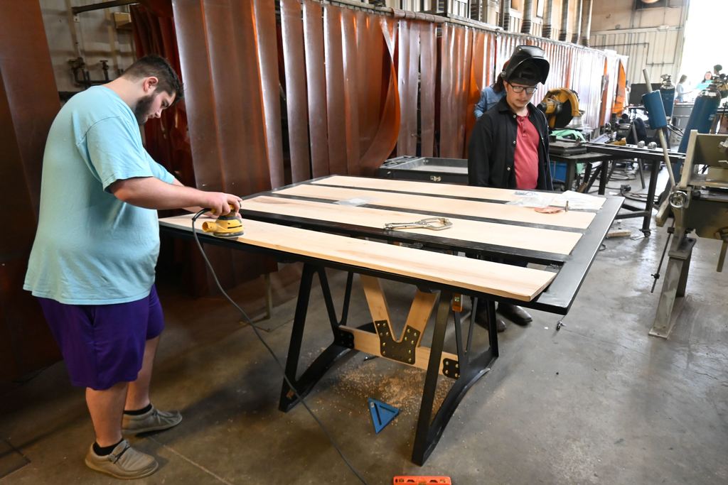 A student sands the wood pieces for a table .