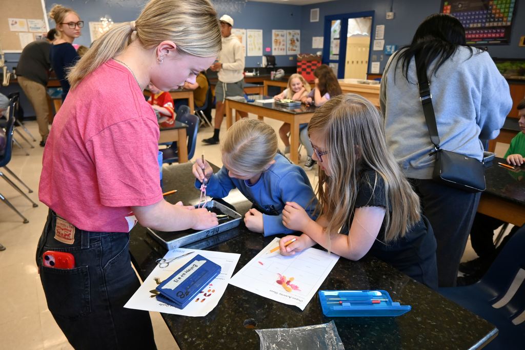 A CNA helps two young girls dissect a frog.