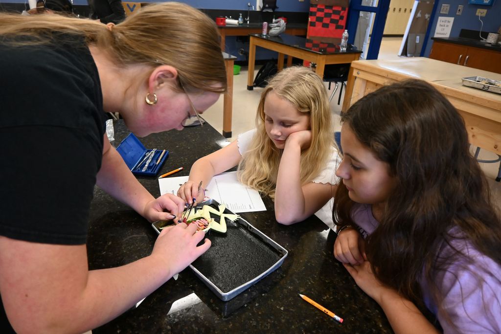 A CNA helps two young girls dissect a frog.