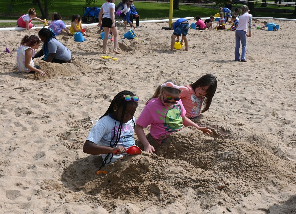 Three girls bury their legs in the sand.