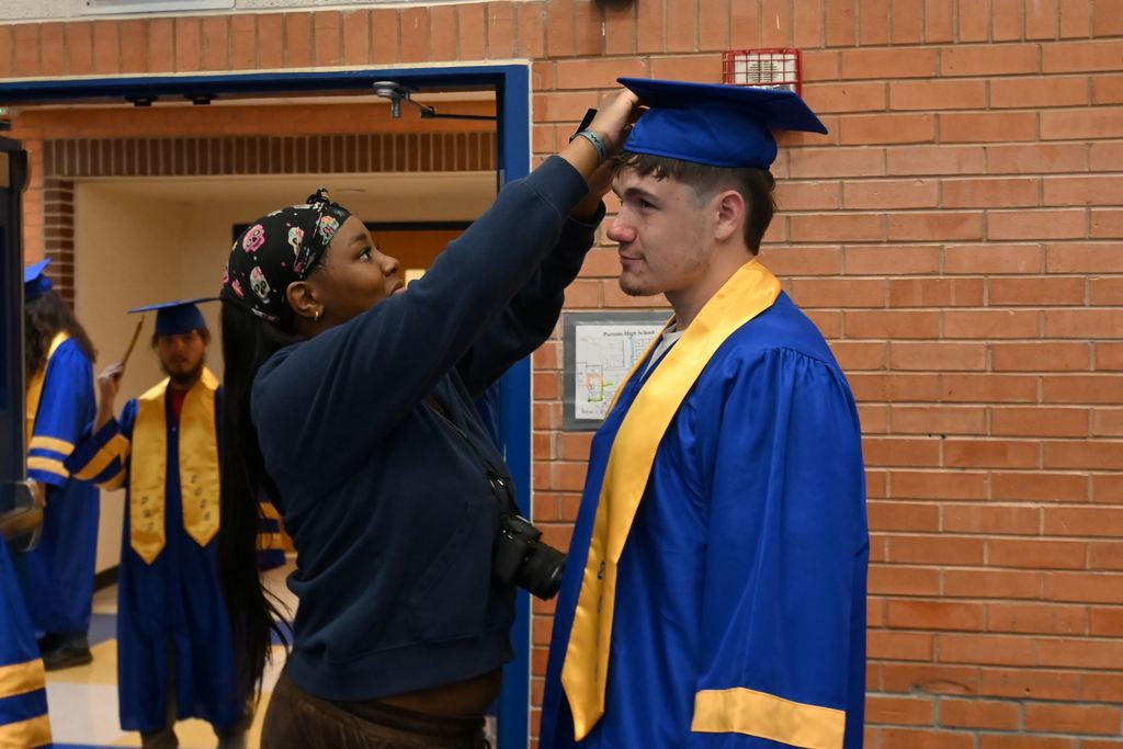 A student photographer adjusts a senior's graduation cap and tassle before taking a photo.