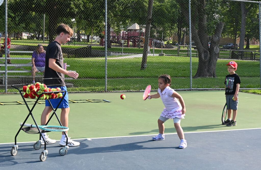 A little girl takes her turn practicing  her forehand.