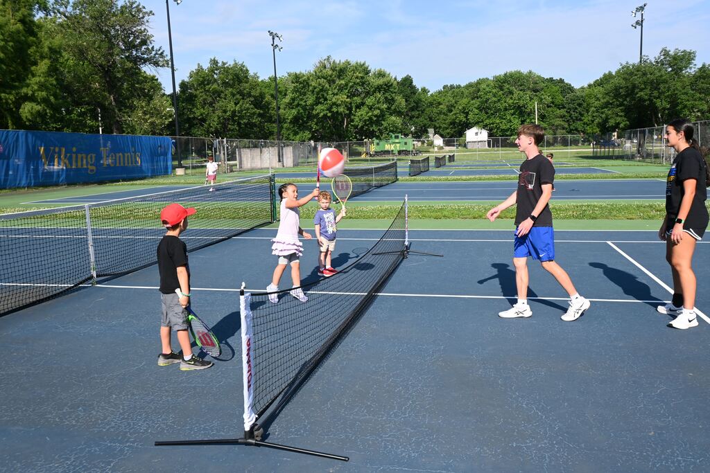 A little girl hits a beach ball with her tennis racquet to return it over the net.