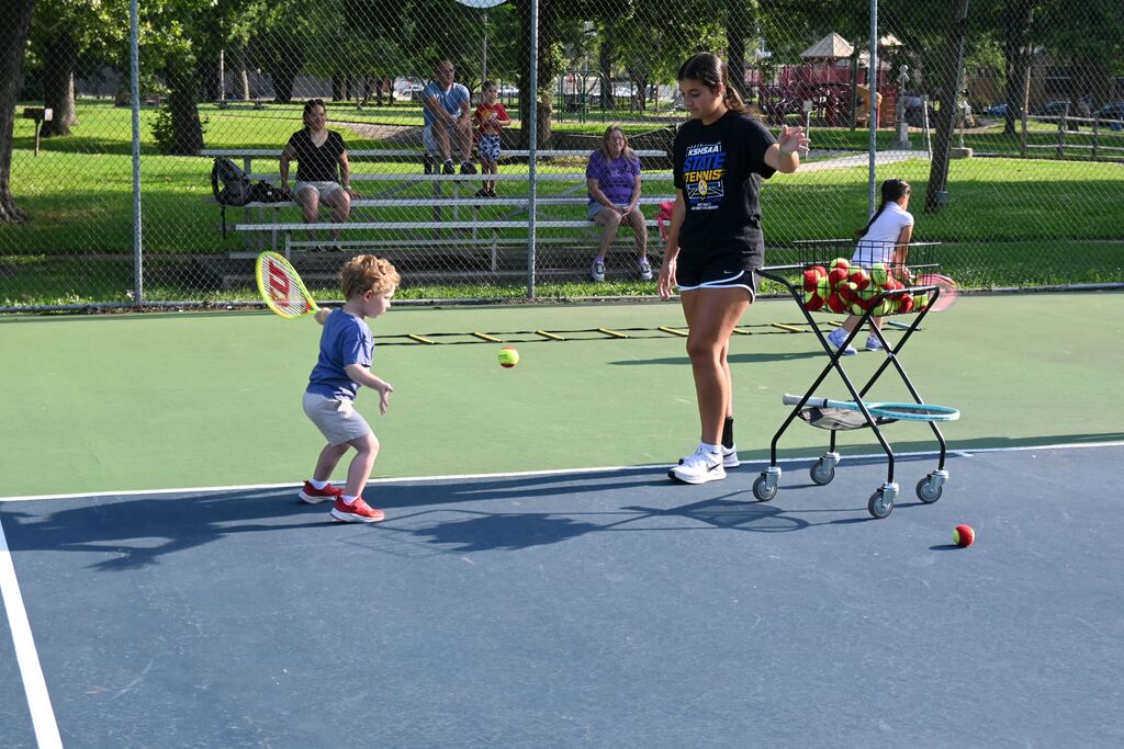 A little boy takes his turn practicing  his forehand.