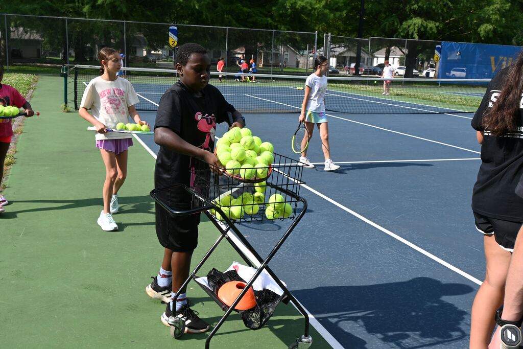 A boy dumps tennis balls he collected from the court into a basket.