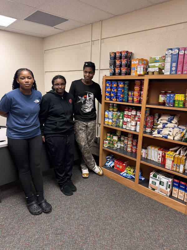 CAMP students stand by shelves they organized and stocked with food.