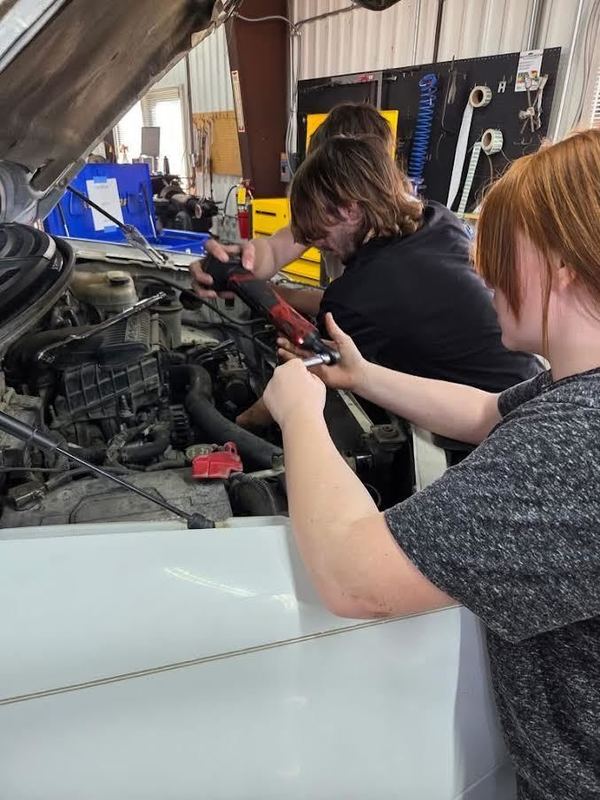 Students work uner the hood of a vehicle in the shop.